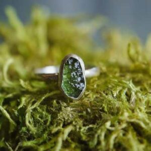 A Moldavite ring on mystic grass with a grounding stone like Smoky Quartz, Black Tourmaline, or Hematite in the setting.