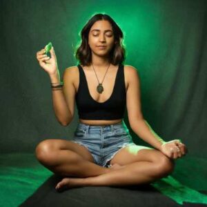 A person meditating in a seated position, holding a piece of Moldavite in their left hand, bathed in a soft green light.