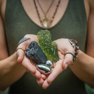 A photo of a person holding a grounding stone in one hand and a Moldavite crystal in the other, with their eyes closed in a grounded, meditative state.