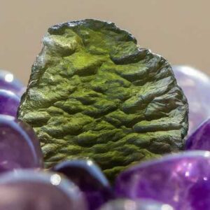 A photo of Moldavite resting on a bed of tumbled amethyst crystals, bathed in soft morning sunlight.